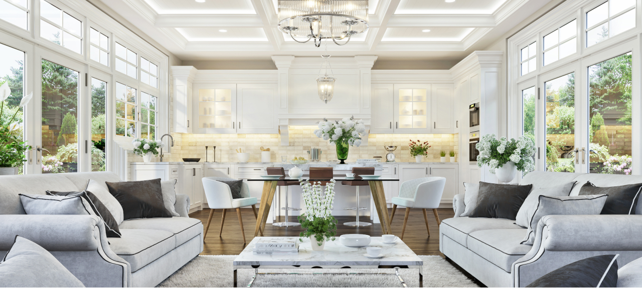 A bright, elegant living room and kitchen combination with large windows, white cabinetry, and plush seating.