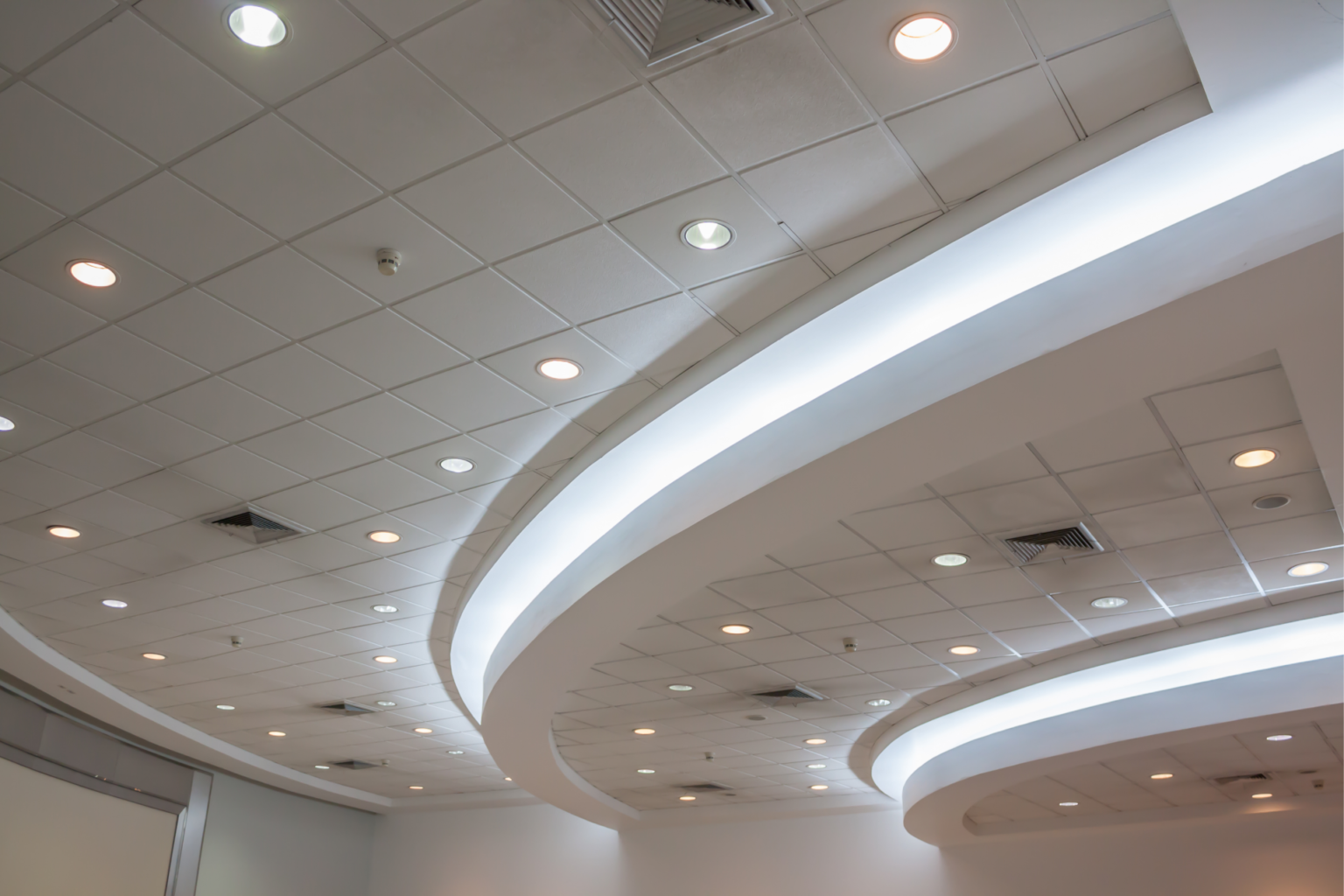 Ceiling with modern recessed lighting and curved architectural features, showcasing a clean and contemporary design with integrated LED light strips.