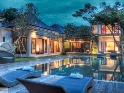 Tropical villa with a serene pool area, surrounded by lush greenery and modern outdoor furniture, illuminated at dusk for a relaxing ambiance.